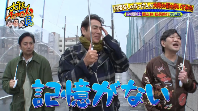 雨の中、傘をさして大阪の街を歩く3人の男性が写っています。テレビ番組「大阪おっさんぽ」の一場面で、宇梶剛士の暴走族総長時代の伝説がテーマのようです。「記憶がない」というテロップが印象的です。