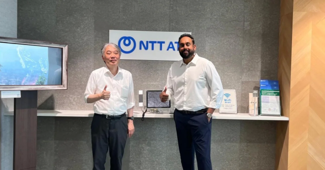 NTT ATのロゴを背景に、2人の男性が笑顔でサムズアップしています